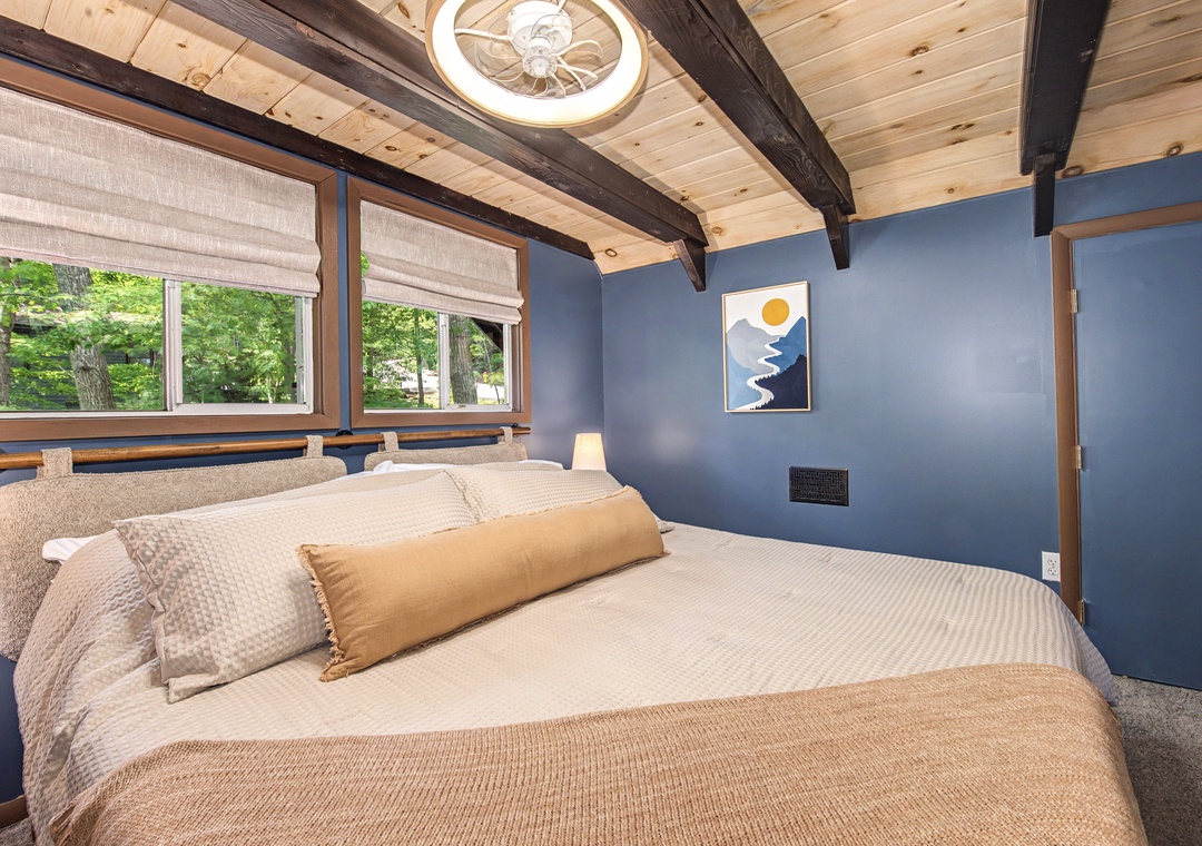 Sink into plush bedding beneath rustic wood beams, with sunlight filtering through treetops. Your serene retreat features calming blue walls and a peaceful forest view.