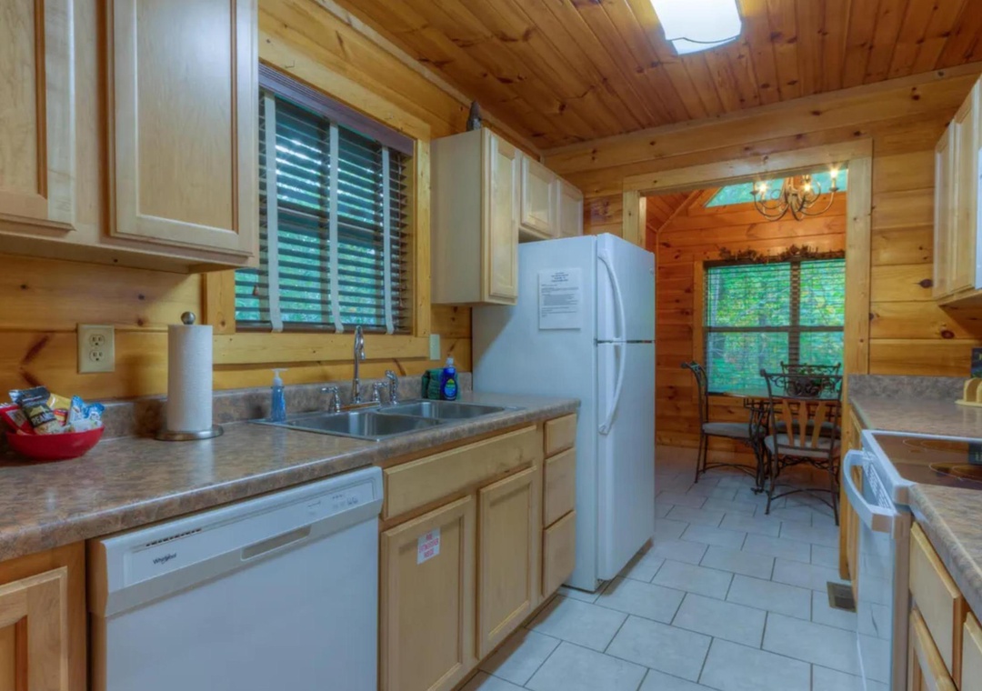 Your fully equipped kitchen features modern appliances, ample counter space, and warm wood accents, opening to a cozy dining nook with forest views through large windows.