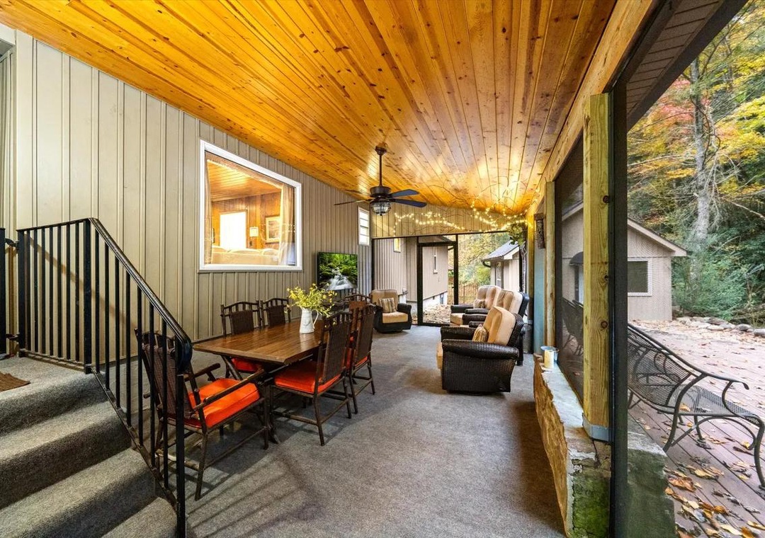 A covered porch with a warm wooden ceiling where you can gather around the dining table or unwind in comfortable seating, all while surrounded by peaceful forest views.