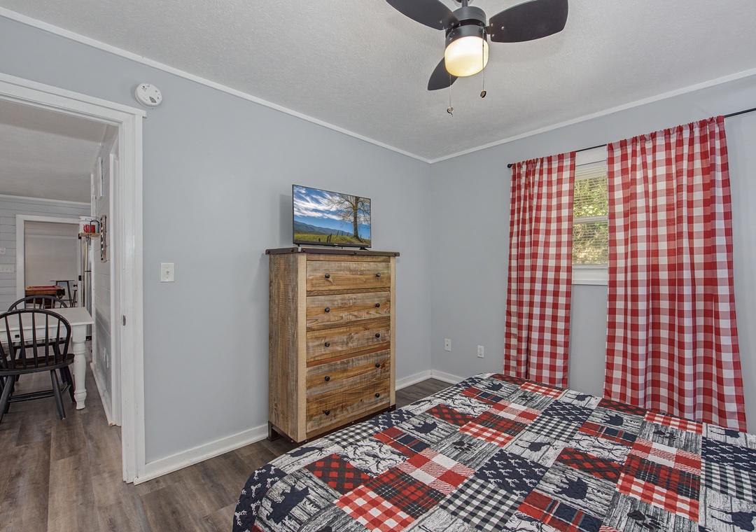 Your cozy bedroom features rustic wood furniture, cheerful red gingham curtains, and a ceiling fan to keep you comfortable year-round.