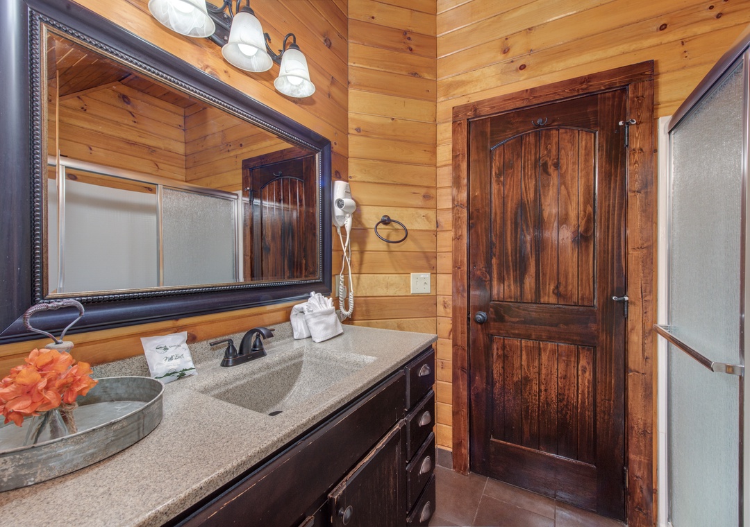 Step into your rustic retreat bathroom with warm wood walls, elegant granite counters, and thoughtful amenities.