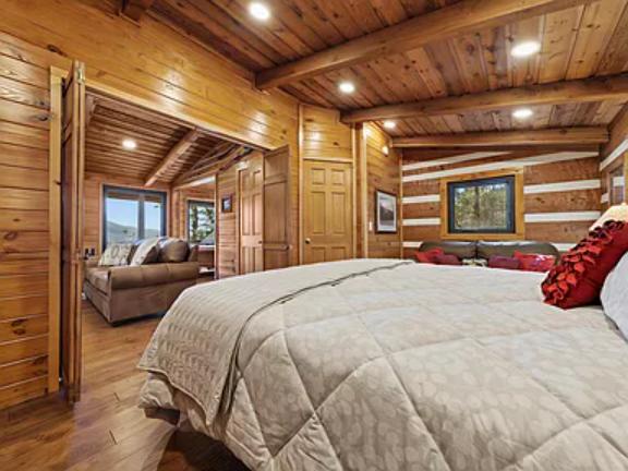 Drift off in this spacious log cabin bedroom, wrapped in soft linens under handcrafted wood beams. Natural light and cozy seating invite you to unwind in rustic mountain charm.
