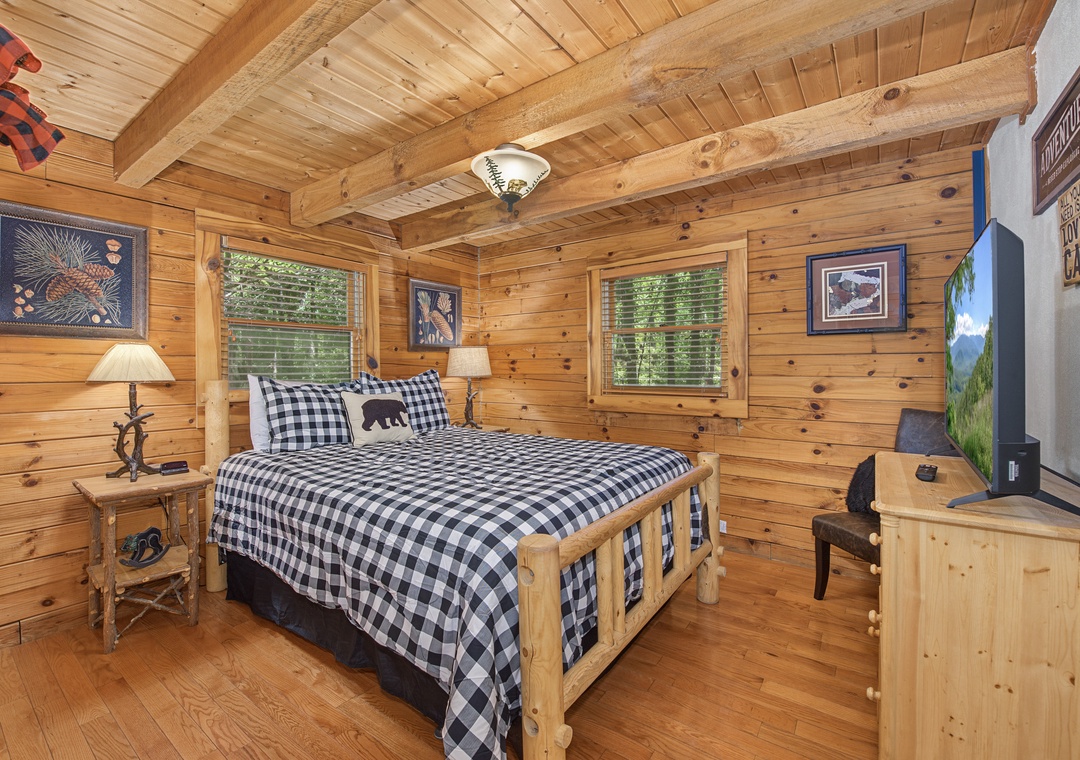 Your cozy cabin bedroom welcomes you with rustic timber beams, warm wood walls, and a handcrafted log bed dressed in cheerful gingham. Natural light streams through the windows, inviting peaceful mountain mornings and restful nights.