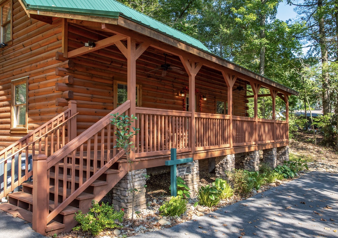 A welcoming log cabin nestled among towering trees, featuring a spacious wraparound porch perfect for morning coffee and evening gatherings. The natural wood and stone foundation blend seamlessly with the lush surroundings.