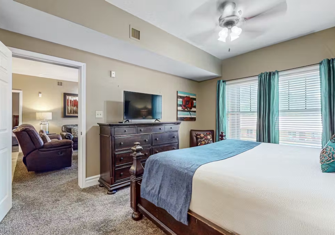 Relax in your spacious bedroom featuring plush bedding, entertainment center, and turquoise accents that create a serene retreat.
