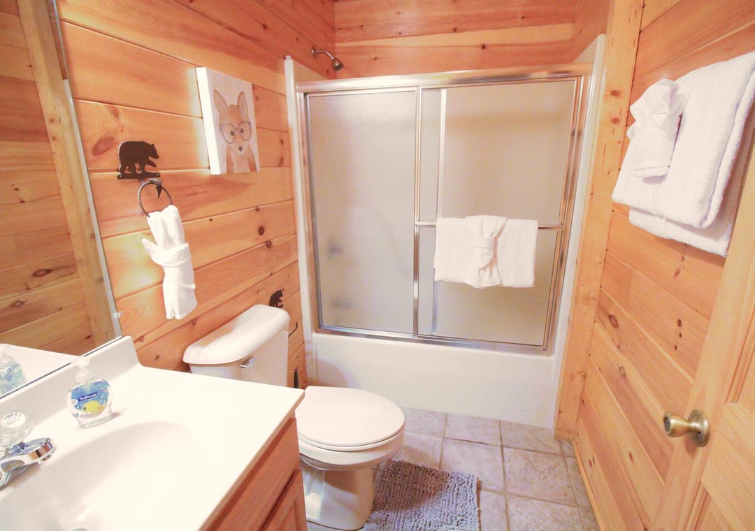 Unwind in your cozy cabin bathroom with warm wood walls, fresh towels, and a relaxing tub-shower combo.