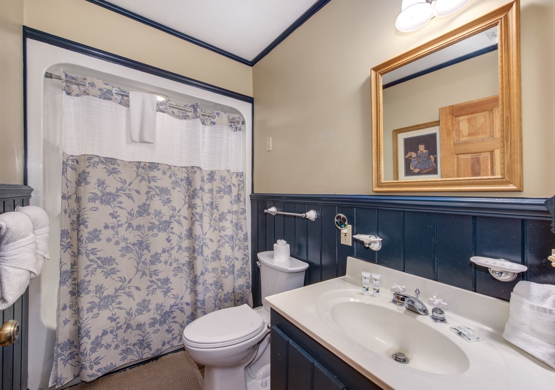 Refresh in your charming bathroom with elegant navy wainscoting, floral curtains, and classic fixtures that blend vintage charm with modern comfort.