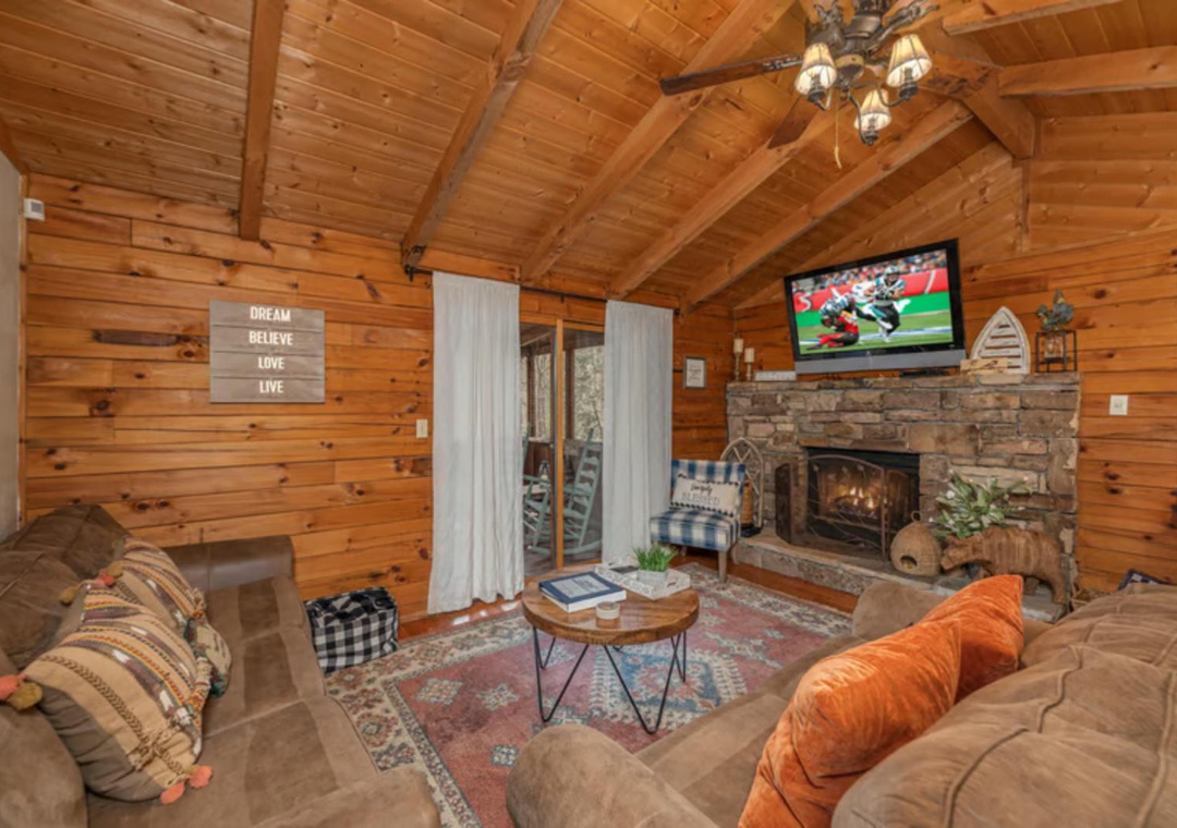 Curl up in this warm wood cabin living room with vaulted ceilings, a cozy stone fireplace, and inviting sofas perfect for relaxing after a day of adventure.