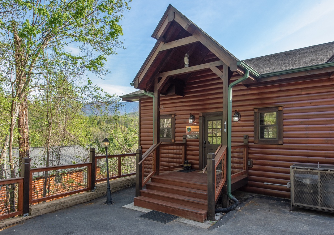 Rustic log cabin entrance welcomes with covered porch and mountain forest backdrop.