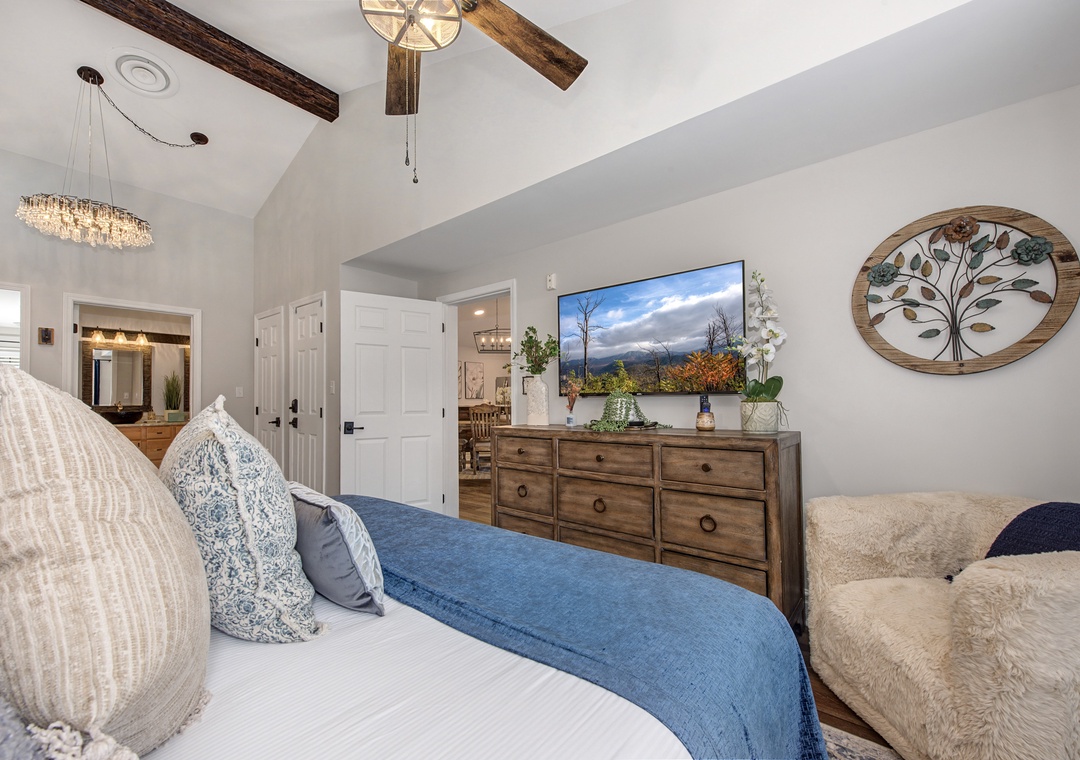 Unwind in your serene bedroom with rustic wooden beams, cozy blue linens, and peaceful mountain views on the wall-mounted TV.