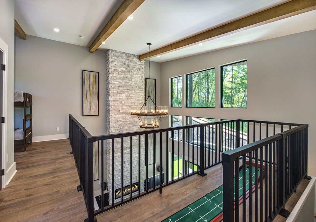 Natural light floods through tall windows, illuminating the open upper level with exposed wood beams overhead. Your mountain retreat features modern design touches throughout, connecting indoor comfort with peaceful forest views beyond.