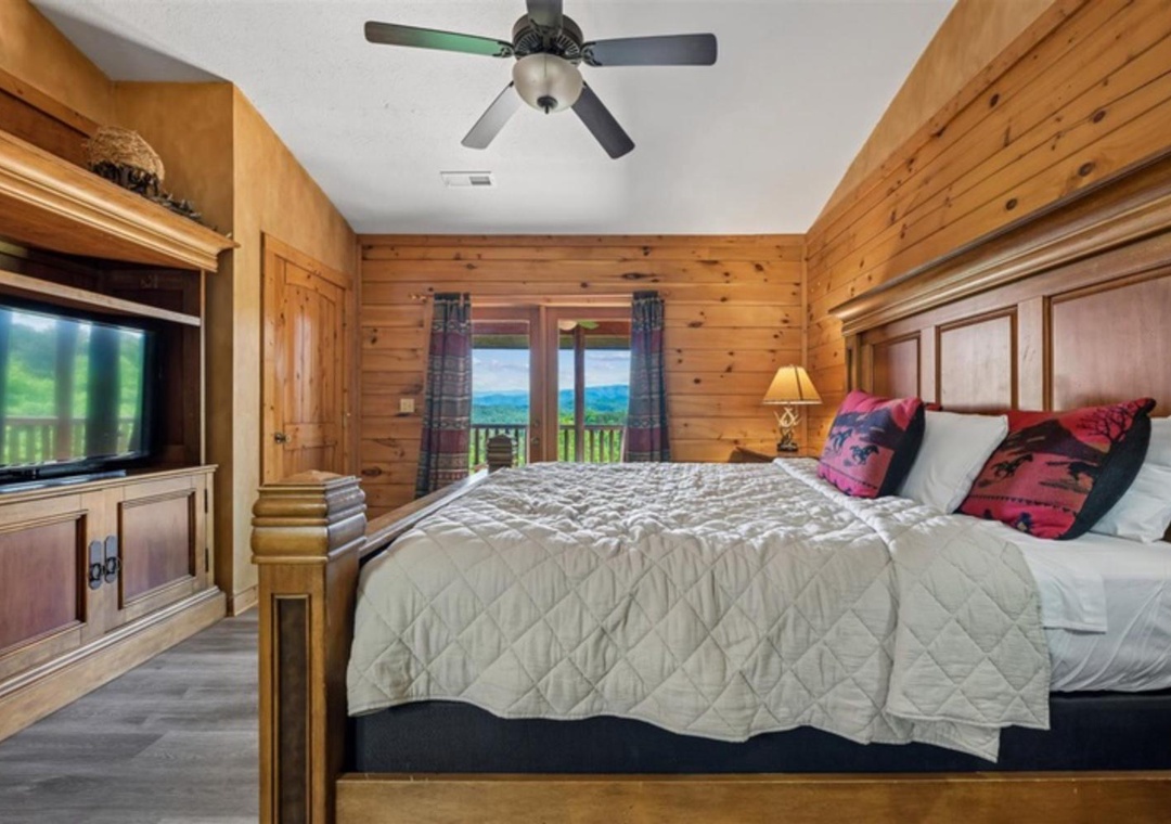 Wake up to stunning mountain views through your private balcony doors. This cozy bedroom features warm wood paneling, a plush king bed, and entertainment center—your perfect retreat after a day of adventure.