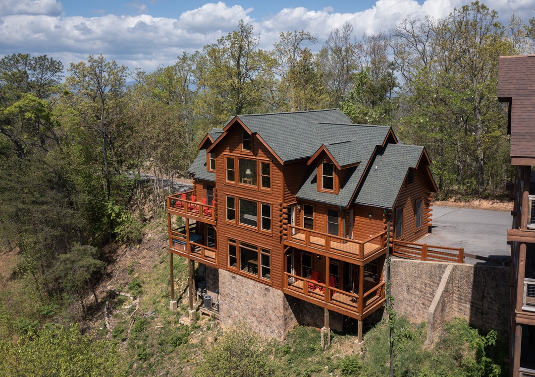 Striking log cabin nestled among mature trees with multiple decks overlooking forested hillside terrain.
