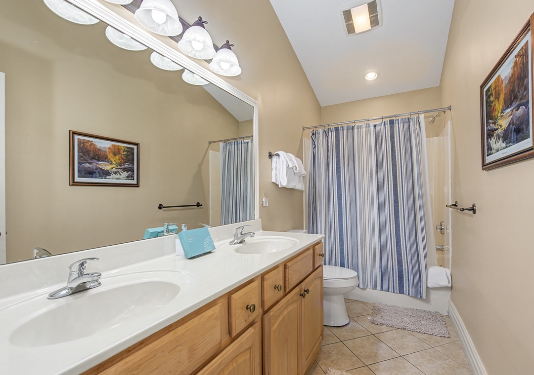 Fresh towels and dual vanities await in your spacious bathroom, with a relaxing tub-shower combo behind crisp blue striped curtains.
