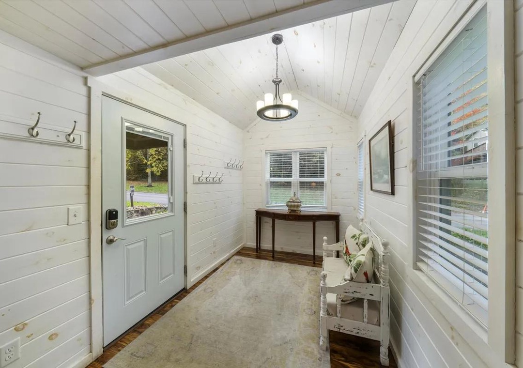 A bright, welcoming entrance with charming white shiplap walls and natural light streaming through windows and glass-paneled door—greeting you as you arrive at your peaceful retreat.