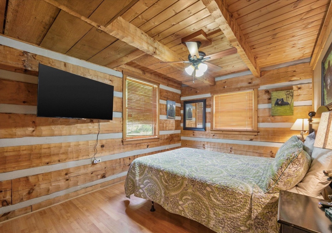 Unwind in this cozy log cabin bedroom where warm wood surrounds you and a ceiling fan ensures your comfort through peaceful nights.