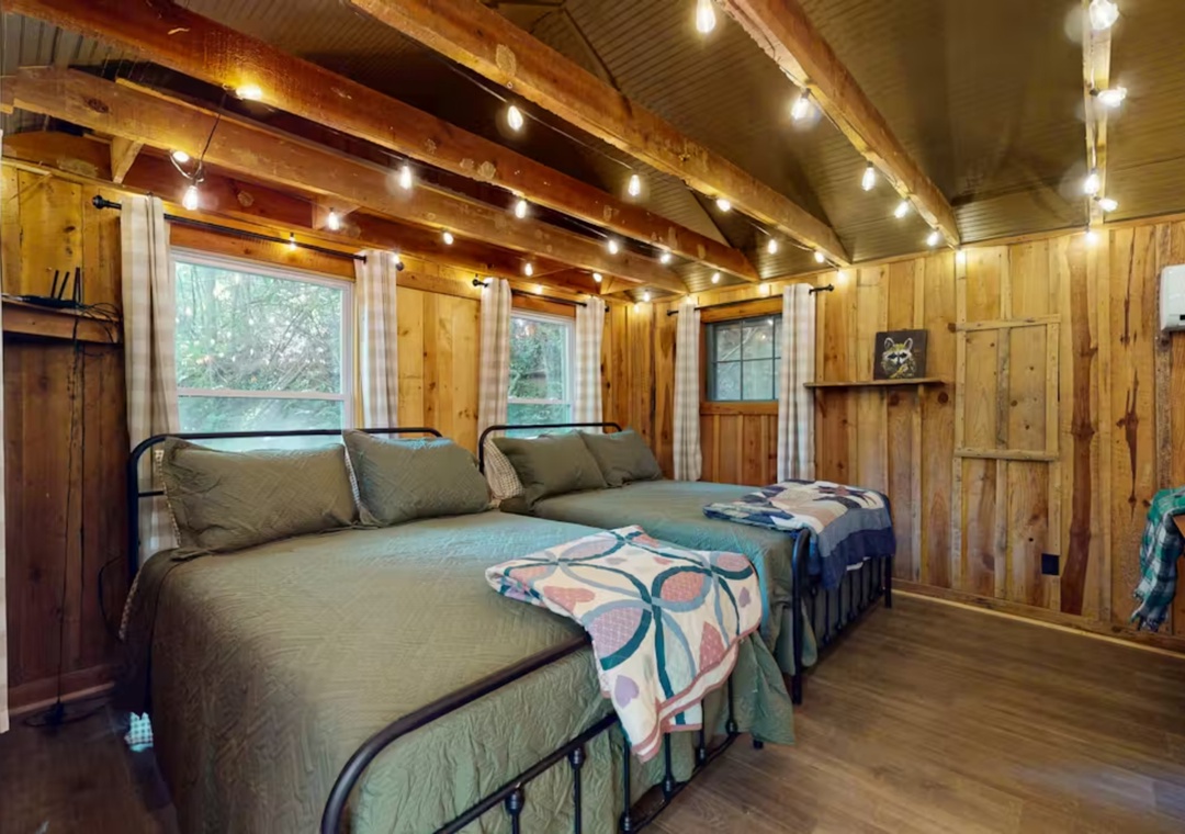 You'll sleep peacefully under twinkling string lights in this cozy cabin bedroom with rustic wood walls and charming twin beds.