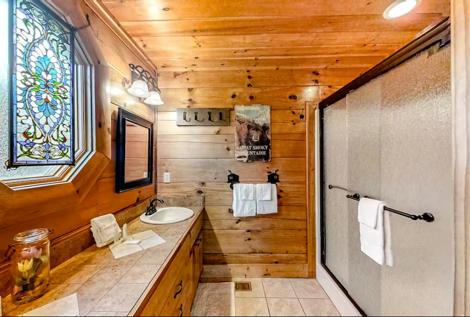 Refresh in your rustic bathroom featuring warm wood walls, stunning stained glass, and a spacious shower with pristine white towels awaiting you.