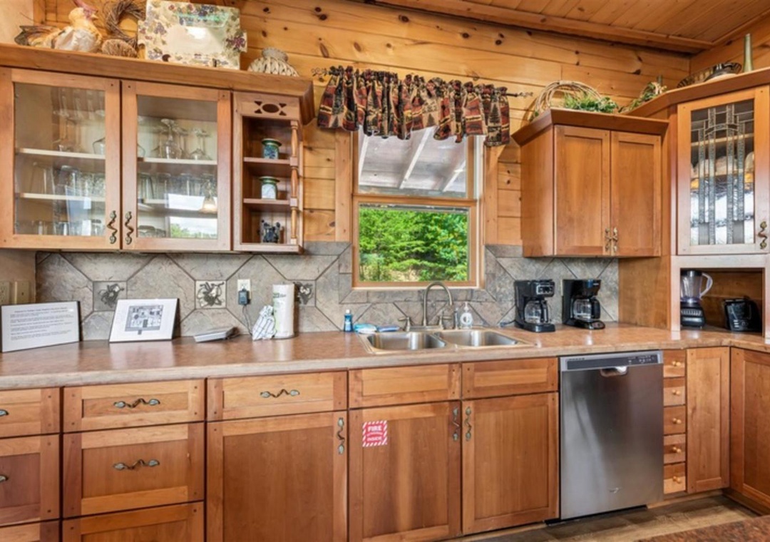 Step into your fully equipped kitchen with warm wood cabinetry, stainless appliances, and a charming window overlooking lush greenery. Everything you need to prepare your favorite meals in cozy, rustic style.