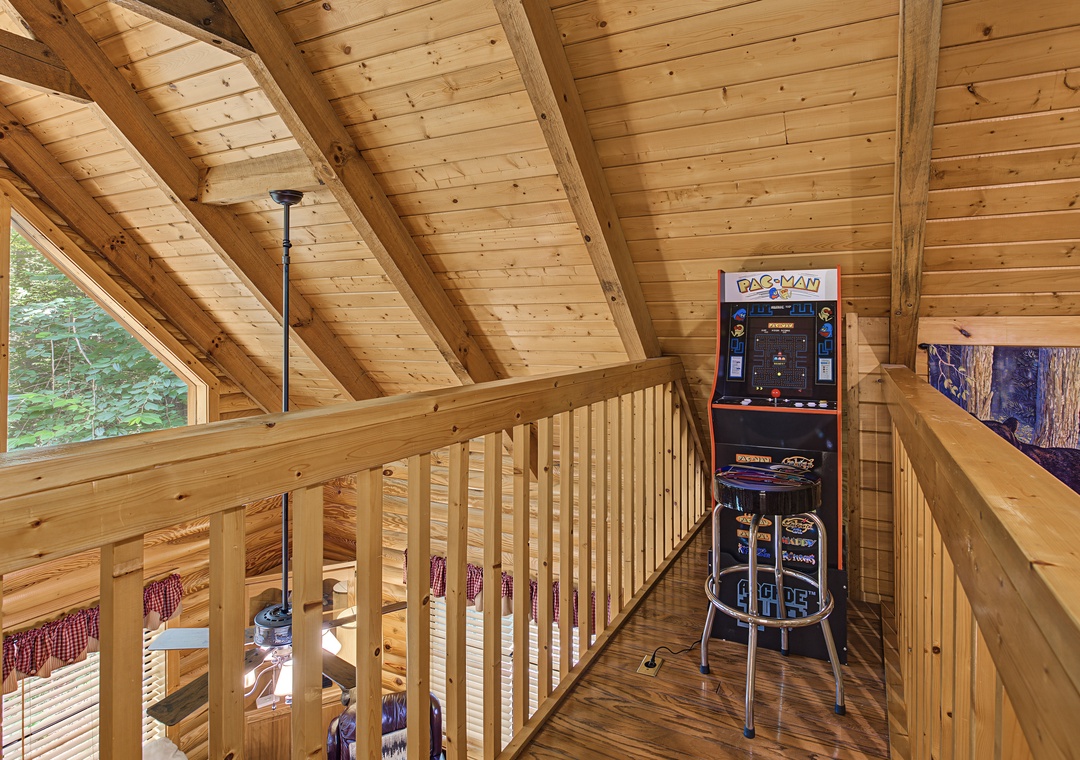 Your loft game room features a classic arcade machine beneath stunning wooden cathedral ceilings, perfect for reliving nostalgic fun while soaking in the cabin's natural charm.
