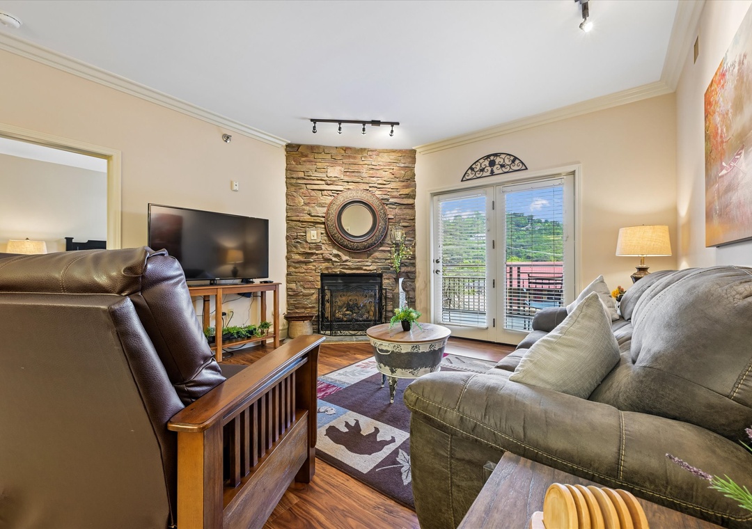Unwind in your inviting living room with a cozy stone fireplace, comfortable seating, and private balcony access offering beautiful mountain views.
