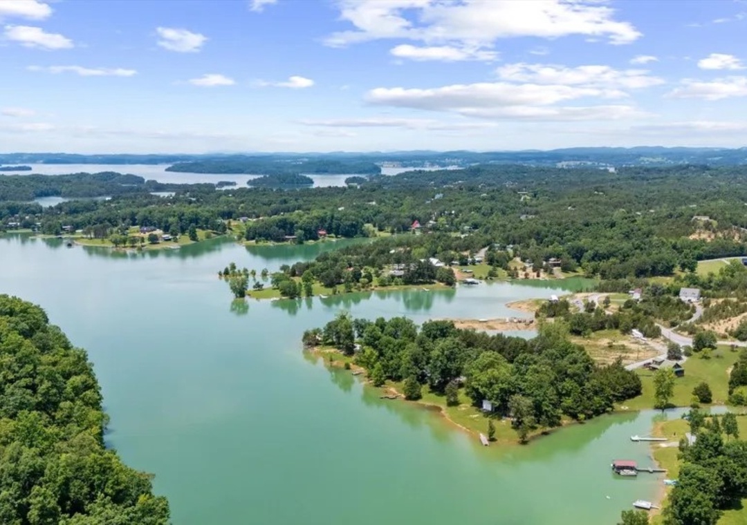 Sweeping aerial view of pristine lakefront community nestled among rolling hills and lush forests.