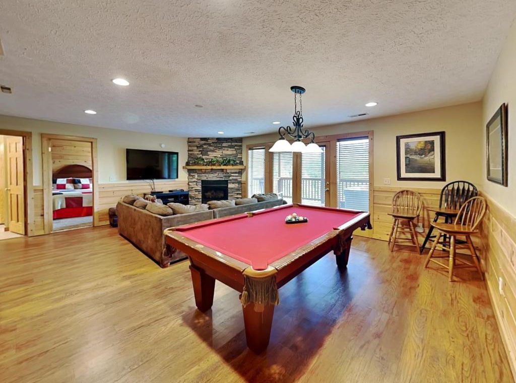 Gather around the red felt pool table for friendly competition while cozy flames dance in the stone fireplace backdrop.