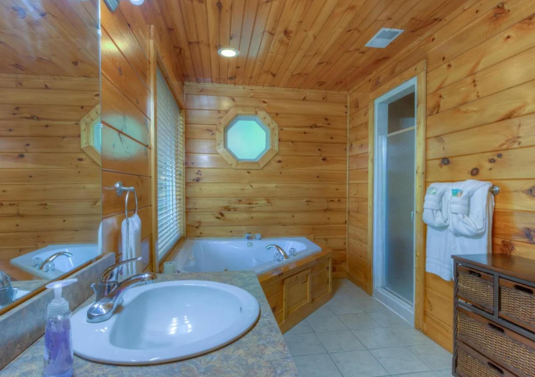 Unwind in your private cabin bathroom, featuring a soothing jetted tub beneath warm wood paneling and a unique porthole window that adds rustic charm.
