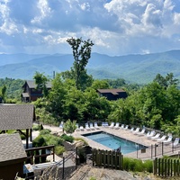 Aerial view of the property showcasing the pool area, lush greenery, and surrounding mountain ranges under a clear blue sky.