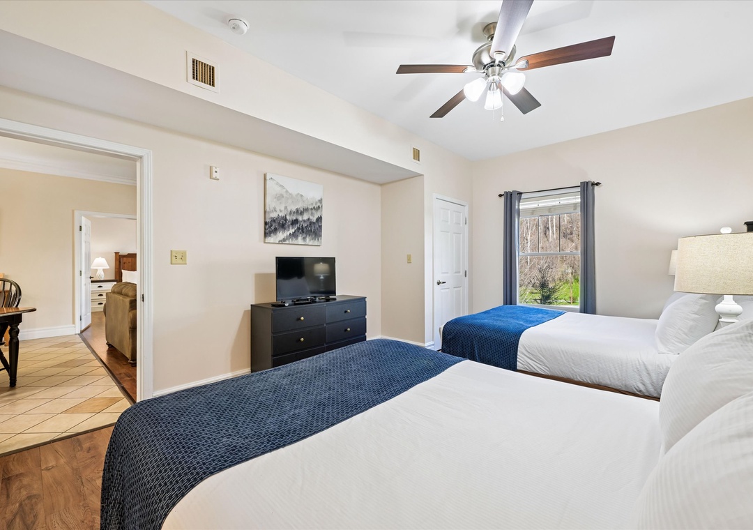 Rest comfortably in your spacious bedroom with two queen beds, ceiling fan, and peaceful woodland views through your window.