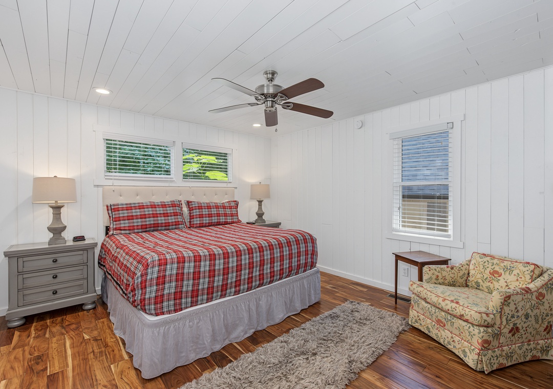 Relax in your cozy bedroom with crisp white shiplap walls, warm wood floors, and a ceiling fan to keep you comfortable year-round. Natural light floods the space through multiple windows, inviting peaceful rest.