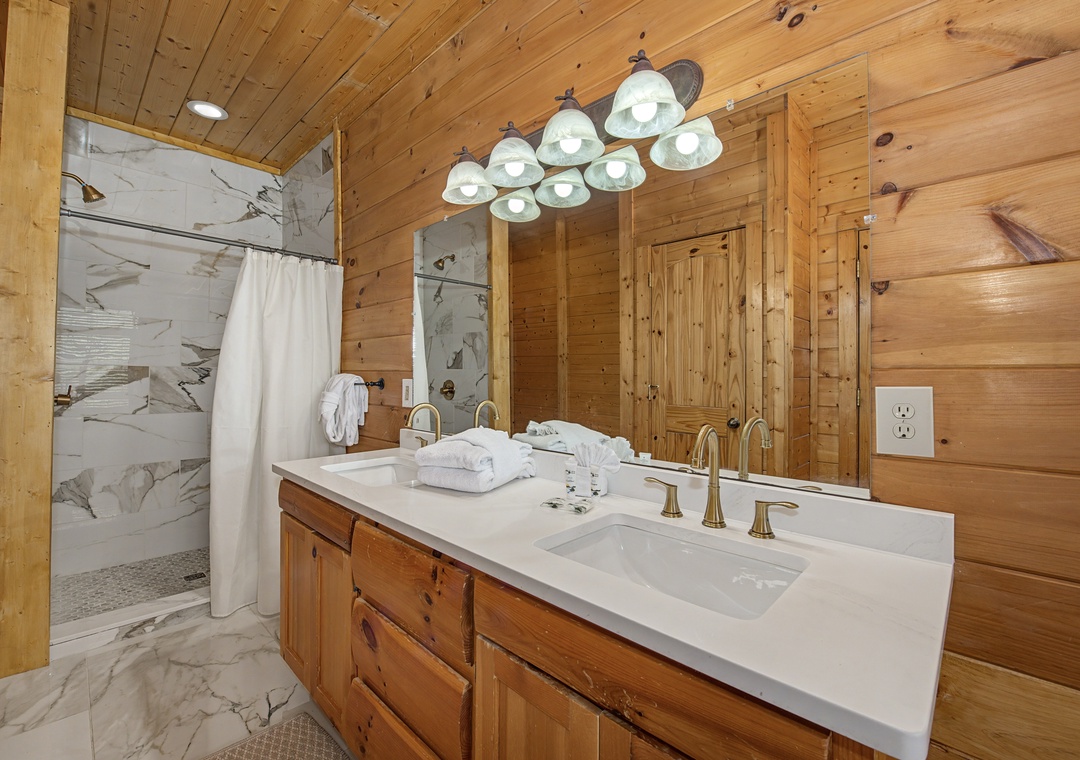 Unwind in your rustic-chic bathroom with warm wood and marble elegance, featuring dual sinks and a rainfall shower.
