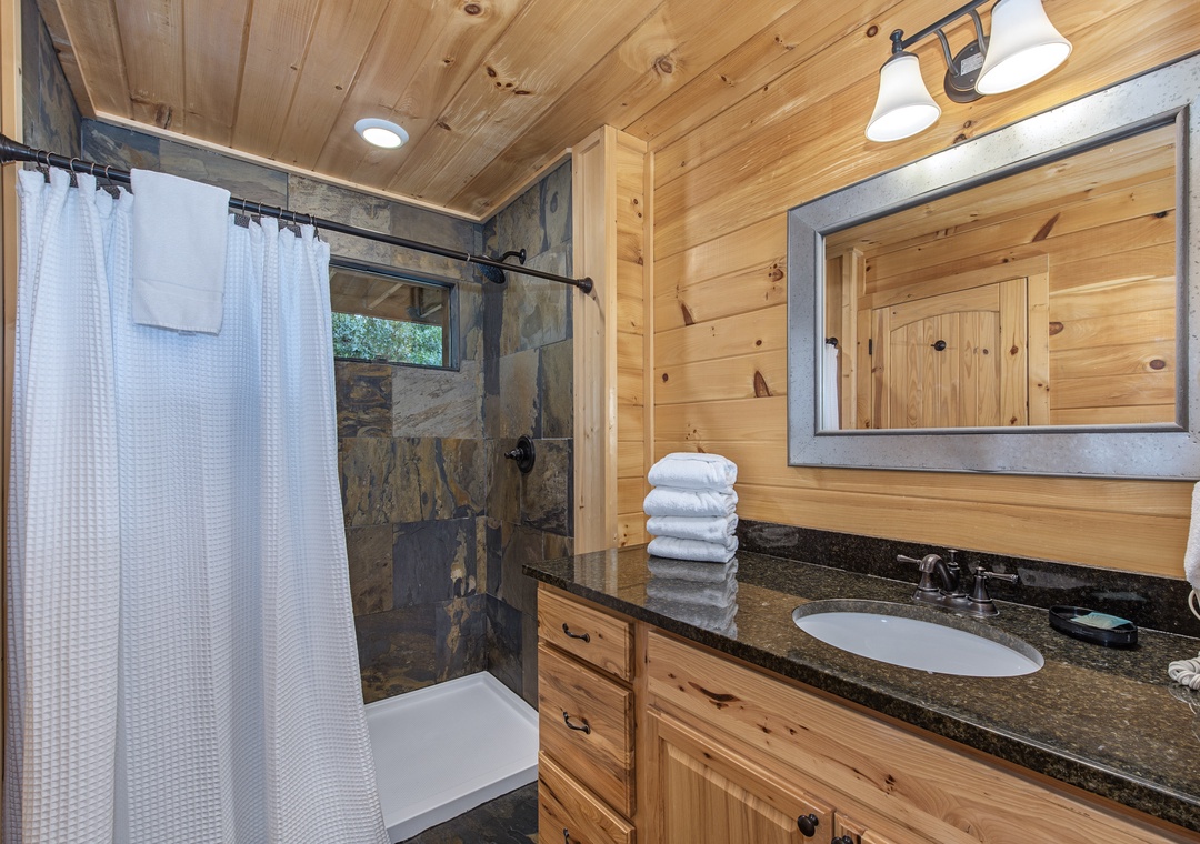Unwind in your cozy cabin-style bathroom featuring a spacious stone-tiled shower, plush towels, and rustic wood finishes that make you feel right at home.