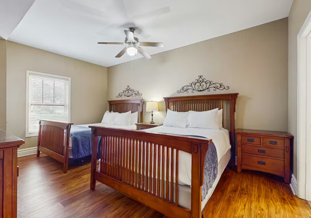 Rest peacefully in your spacious bedroom featuring twin beds with rich wood furnishings, ceiling fan comfort, and warm hardwood floors.