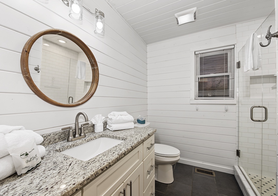 Step into your serene coastal-inspired bathroom, where shiplap walls and a warm wood mirror create a calming retreat. Fresh towels await you by the granite vanity, and your private glass-enclosed shower promises a refreshing start to each day.