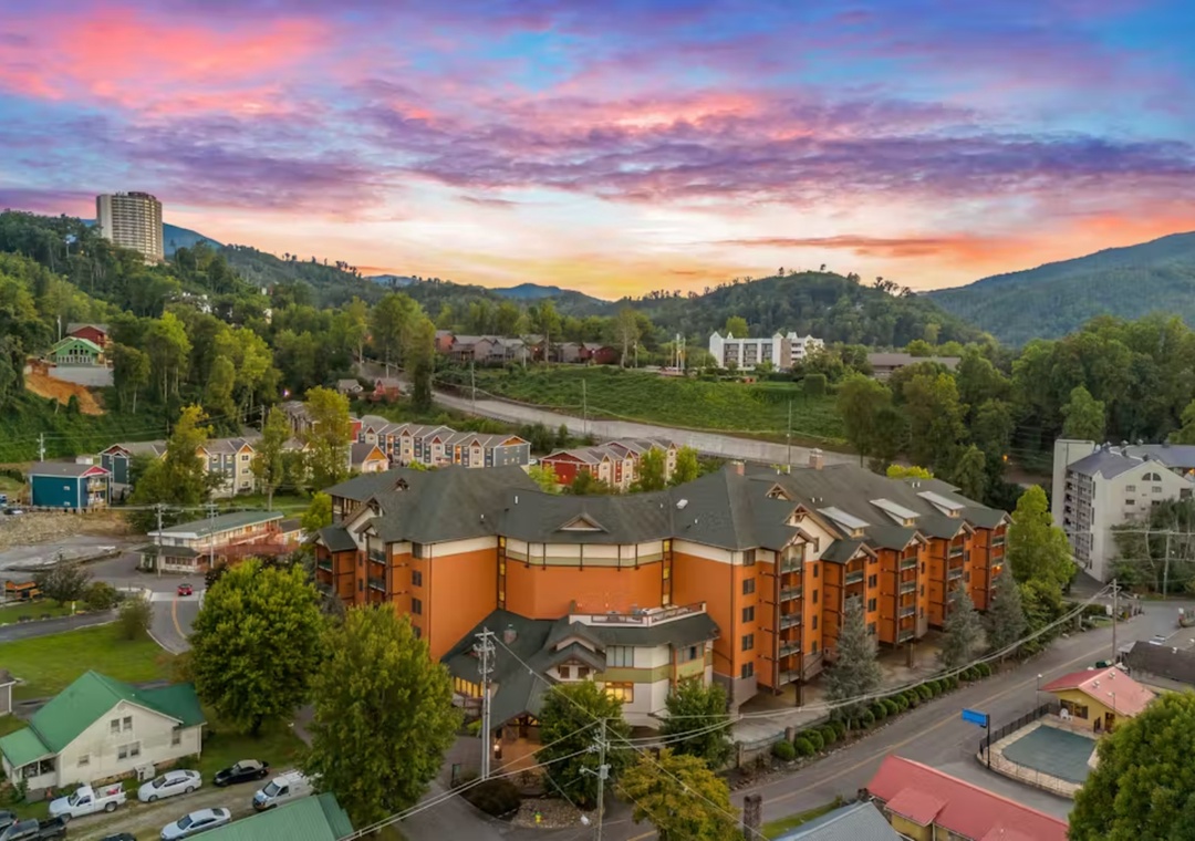 Mountain resort nestled in scenic valley with vibrant sunset skies painting the surrounding peaks and forested hills.