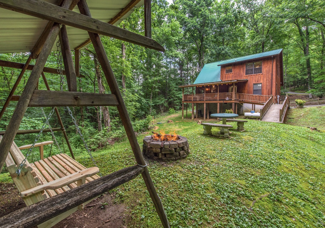 Charming wood cabin nestled in lush forest with a crackling fire pit, garden seating, and a peaceful swing inviting quiet moments under towering trees.