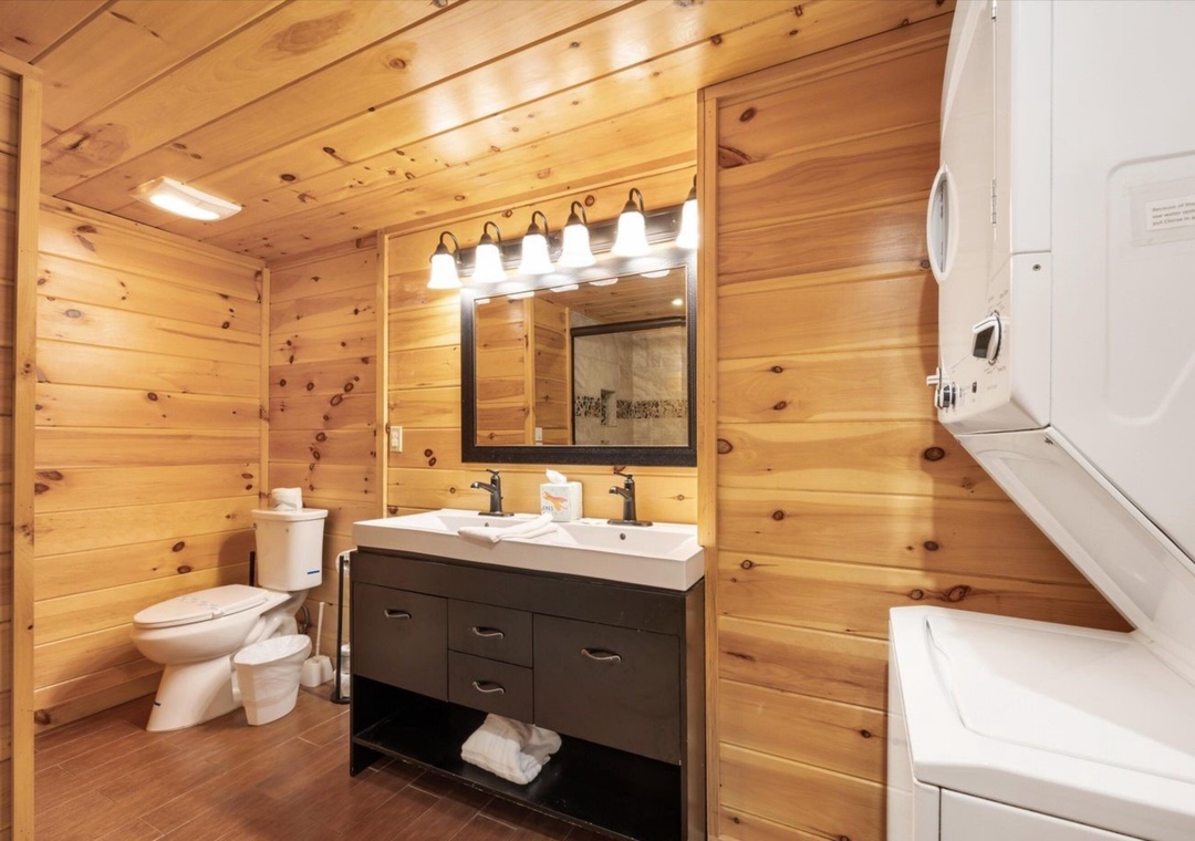 Step into your rustic-modern bathroom with warm wood walls, bright vanity lighting, and pristine white fixtures for a cozy mountain retreat feel.