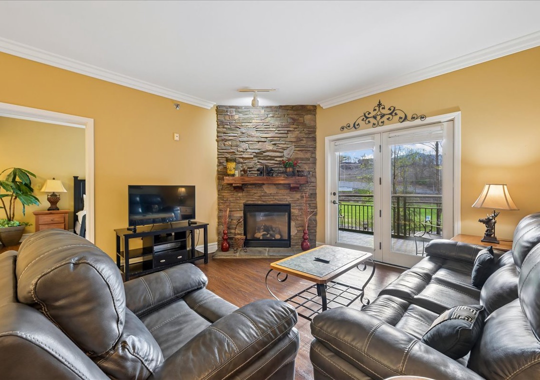 Sink into plush leather seating by your cozy stone fireplace, where warm golden walls and French doors invite relaxation.