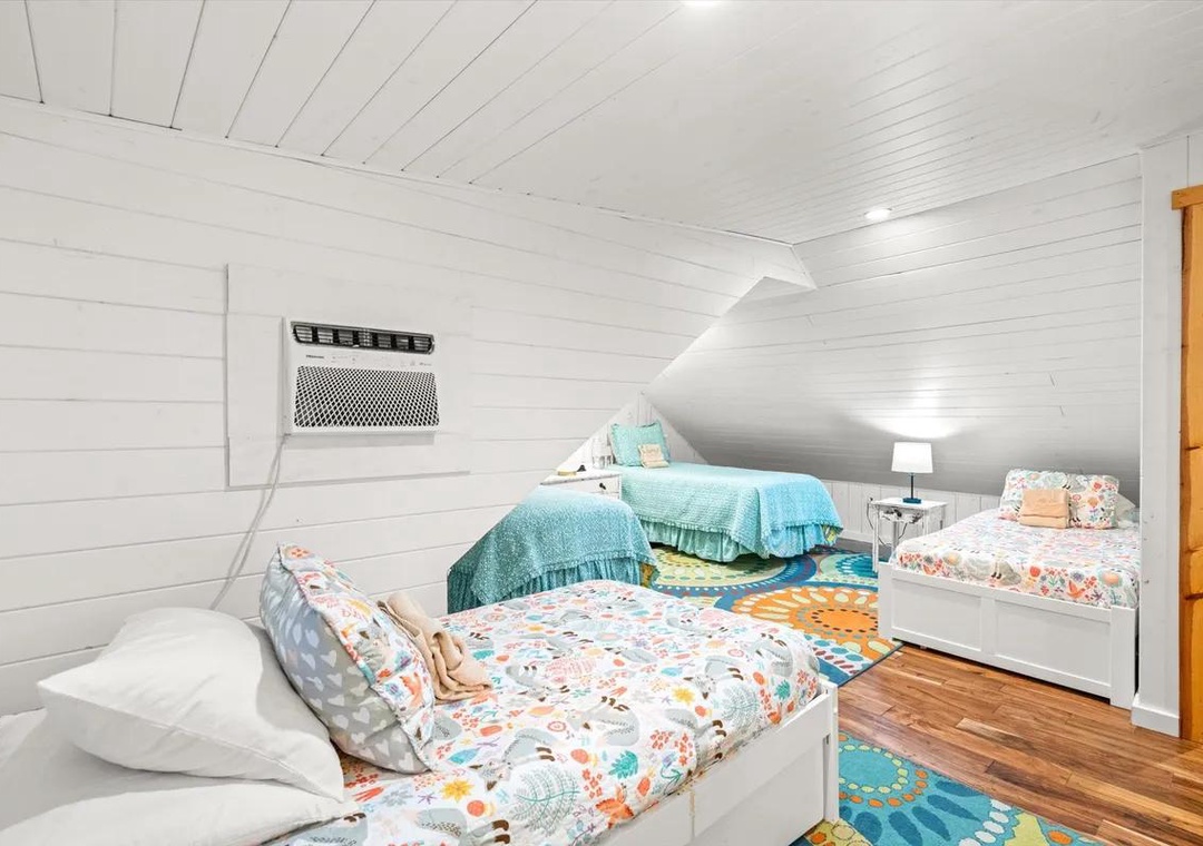 Cozy up in this charming loft bedroom with two comfortable beds, perfect for kids or friends. The bright shiplap walls and colorful accents create a welcoming space where you'll enjoy peaceful nights under the sloped ceiling.