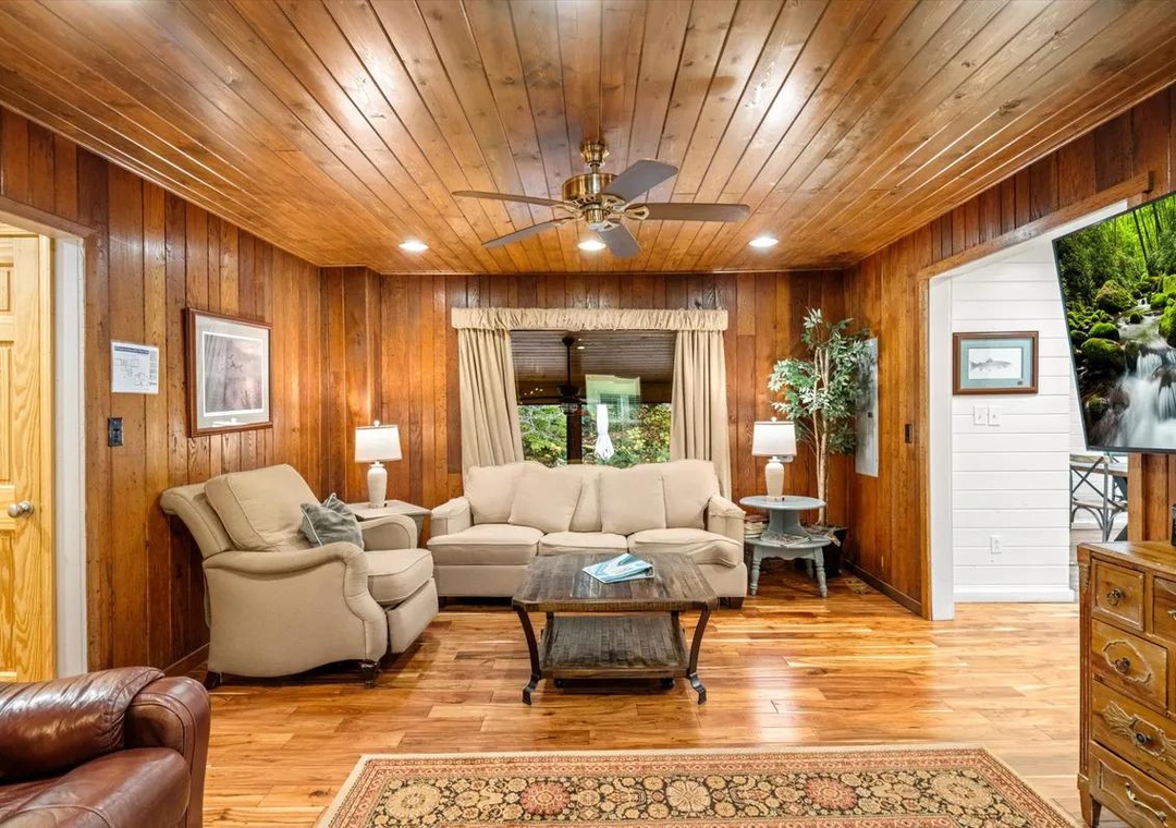 Unwind in your cozy living room, where warm wood paneling and comfortable seating create the perfect retreat after a day of adventure. Natural light filters through the windows while the ceiling fan keeps you comfortable year-round.