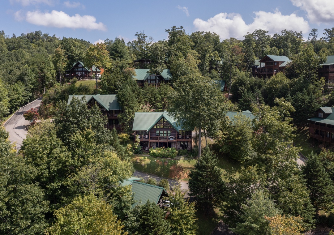 Aerial view of a mountain cabin resort community nestled among dense forest canopy with green metal roofs and rustic architecture.