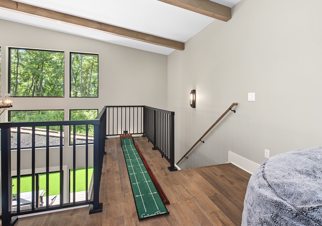 A lofted space with soaring vaulted ceilings and exposed beams opens to forest views through expansive windows. The wooden handrails and thoughtful layout create a unique retreat within your rental.