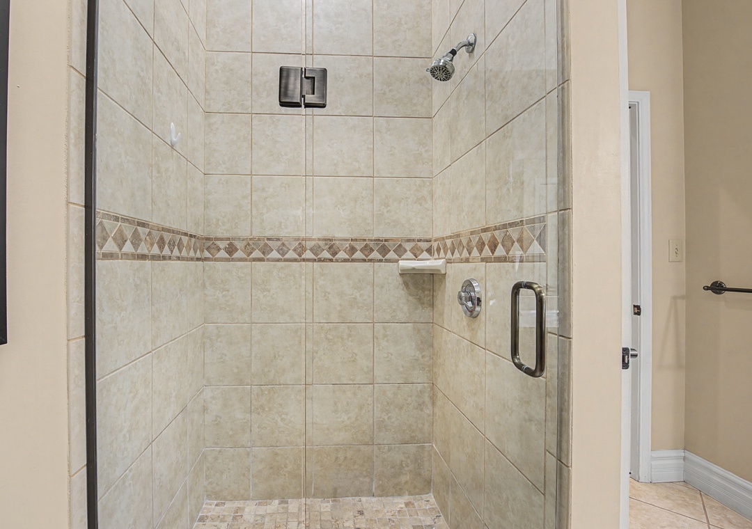 Step into your spacious tiled shower with decorative accent border and rainfall showerhead for a refreshing start to your day.