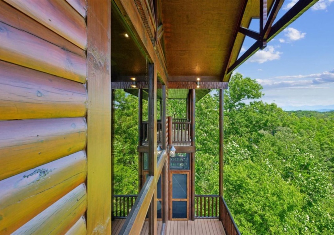 Expansive mountain vistas stretch endlessly from this elevated perch, framing lush green forests and distant peaks under clear blue skies—a scenic backdrop that defines the surrounding area.