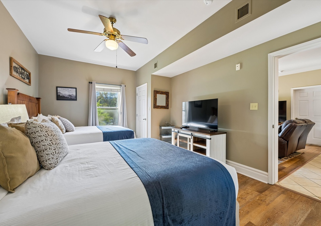 Unwind in your spacious bedroom with two comfortable beds, modern TV, and gentle ceiling fan creating the perfect retreat.