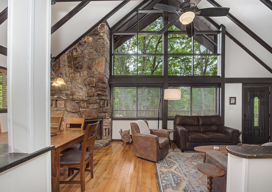 Picture yourself unwinding in this stunning vaulted living room, where exposed beams and a grand stone fireplace create a cozy yet spacious retreat. Natural light pours through tall windows, inviting you to relax.
