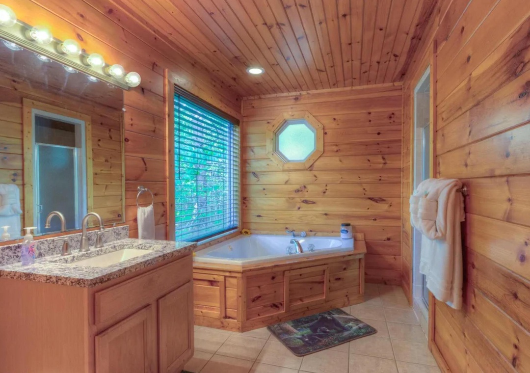 Unwind in your private spa-like bathroom with a luxurious soaking tub set beneath warm wood paneling and soft natural light, where plush towels await your relaxation.