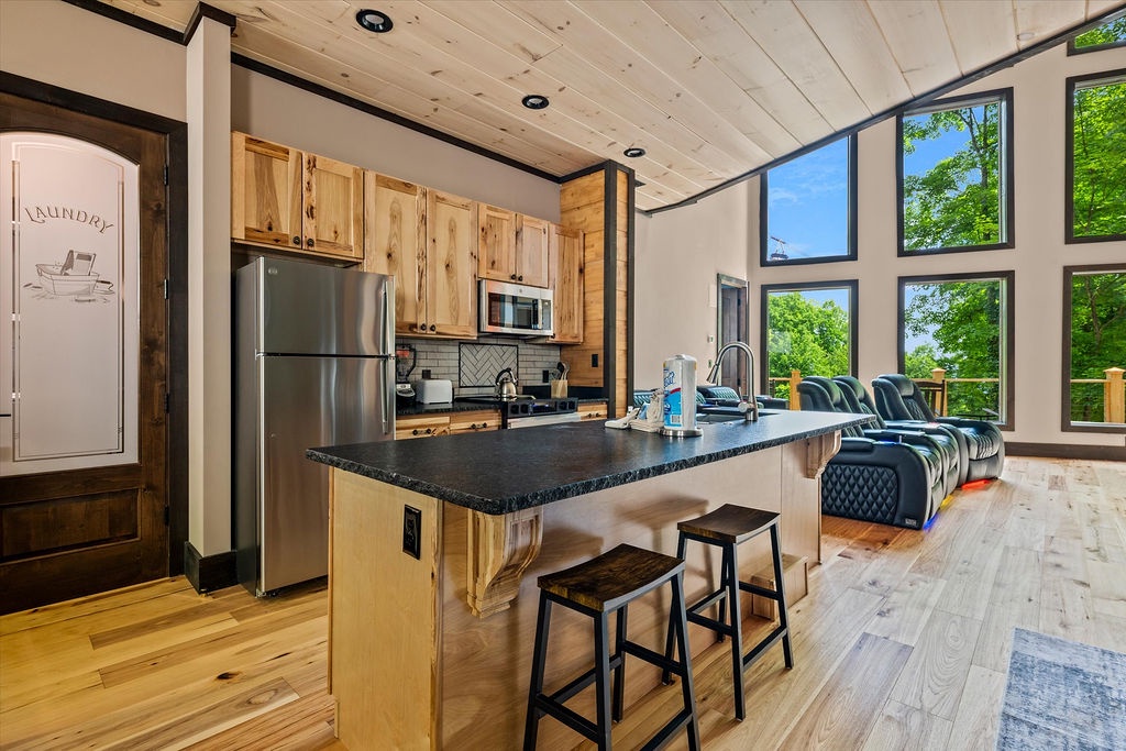 Your open-concept retreat features a fully equipped kitchen with modern appliances and a granite island, flowing seamlessly into a bright living space framed by soaring windows overlooking lush greenery.