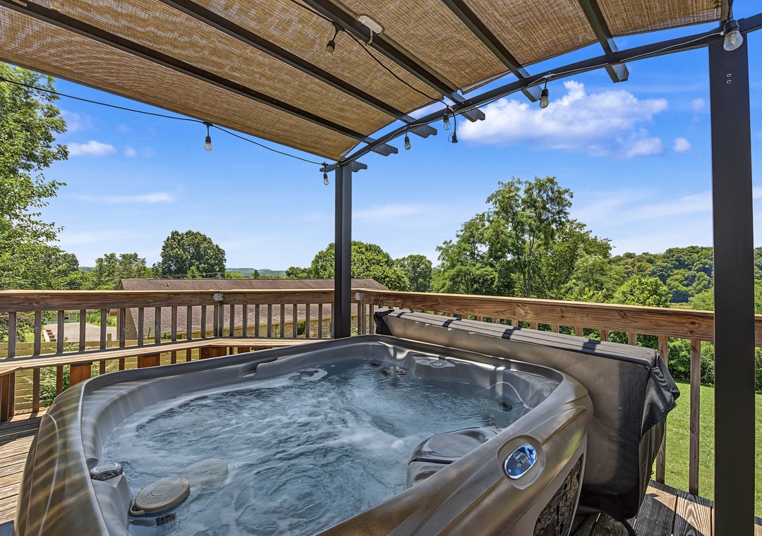 Picture yourself unwinding in this private hot tub under a shaded pergola, surrounded by lush green hills and open sky—pure relaxation awaits.
